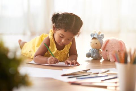 Young child lying on the floor and coloring pages with crayons